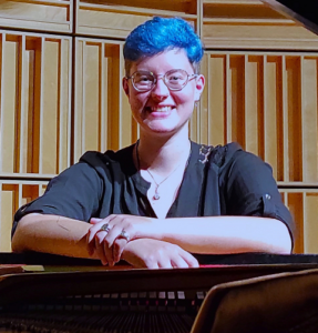 Marina Machado, Interim Music Director of UUFBR, poses behind an open grand piano